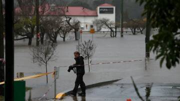 A local snaps a photo of the flooding in Camden, while Enzos Cucina remains underwater behind him. Picture: Sylvia Liber